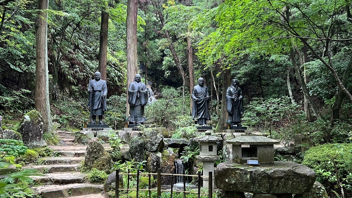 Statues de pierre bouddhistes sur des marches couvertes de mousse, entourées de grands cèdres