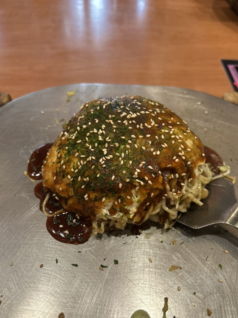 Okonomiyaki de Hiroshima sur une plaque teppan ronde, nappé de sauce, d'aonori et de graines de sésame