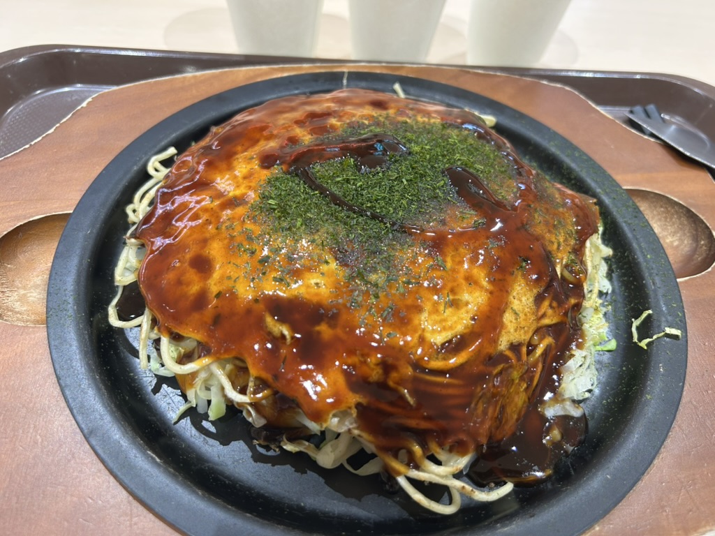 Okonomiyaki de Hiroshima servi sur une plaque en fonte ronde posée sur un plateau de restaurant